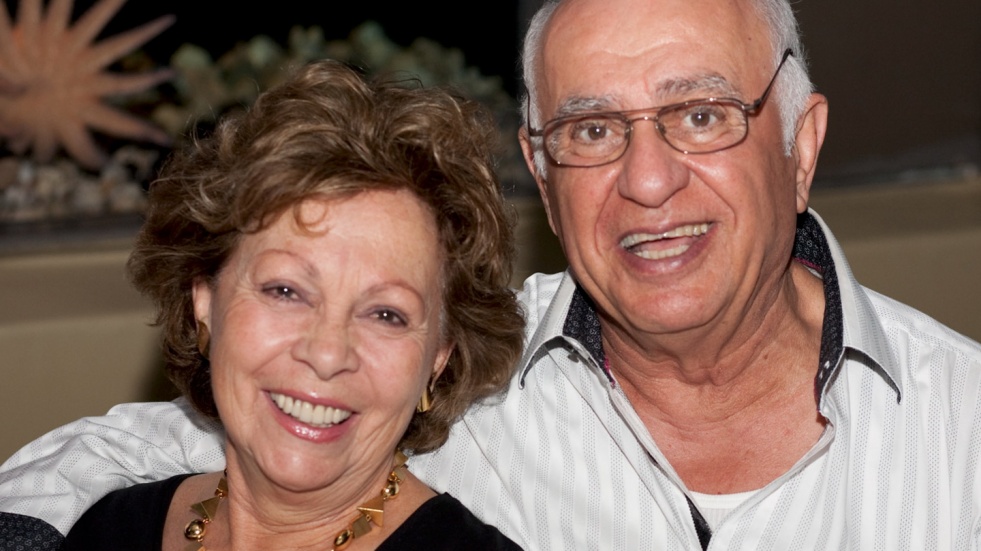 Un couple &acirc;g&eacute; est debout c&ocirc;te &agrave; c&ocirc;te, souriant joyeusement devant l&rsquo;objectif