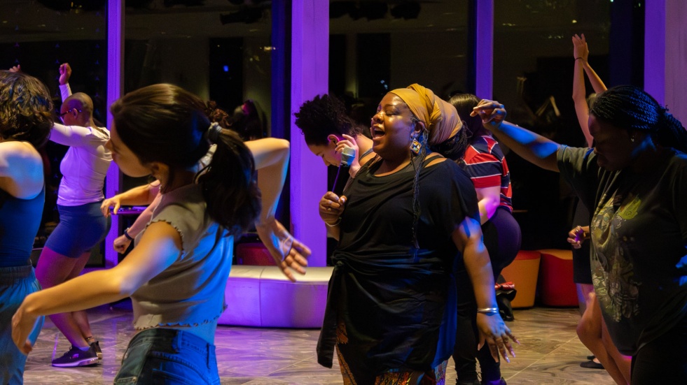 Une femme avec un micro est  entour&eacute;e de danseuses et de danseurs.