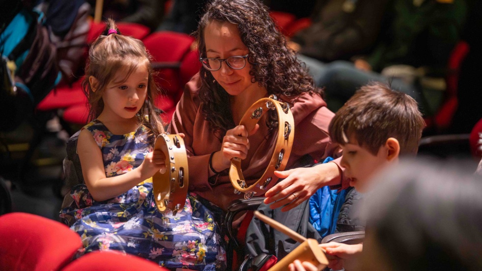 A woman and two young children hold musical instruments.