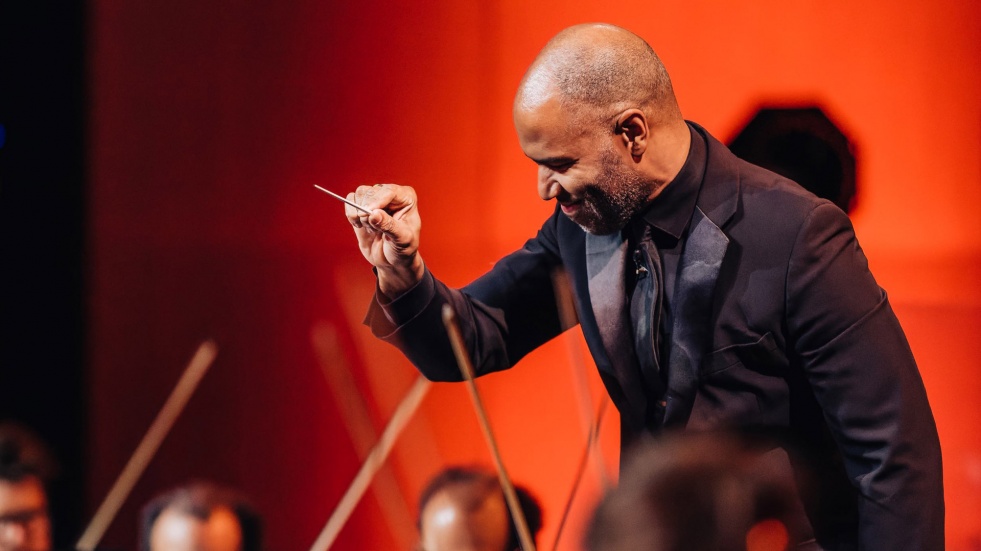 A conductor leads an orchestra on stage.