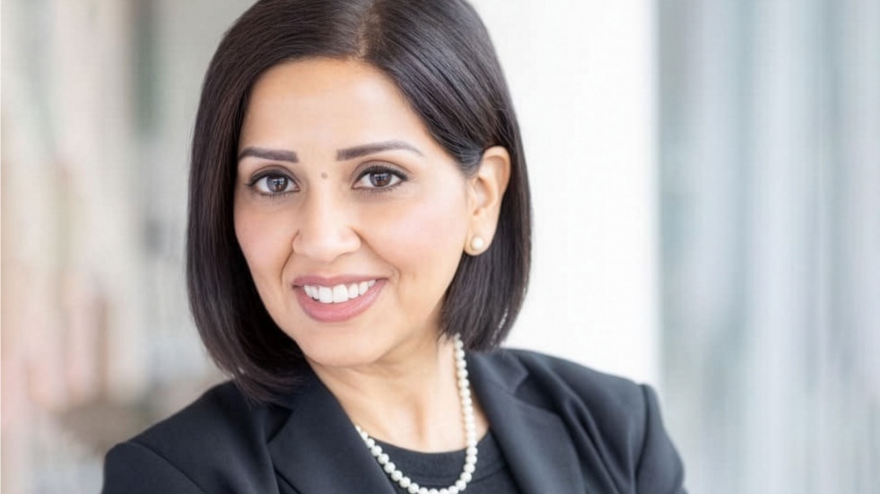 Professional headshot of a woman with short dark hair, wearing a black blazer, black top, and a pearl necklace.